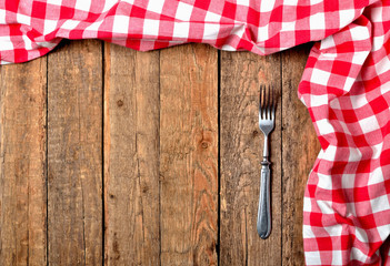 Red checkered tablecloth top and right frame and fork on vintage wooden table background - view from above