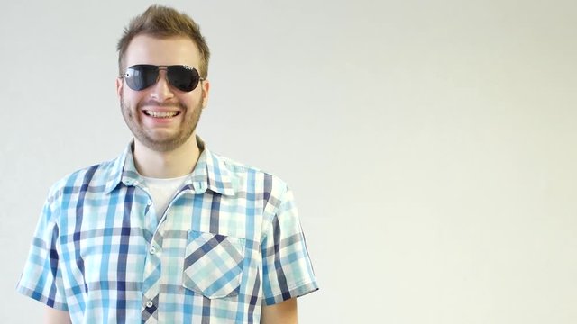 Young stylish unshaven caucasian man in black glasses is standing smiling and looking at the camera, close-up, white background, copy space, fashionable