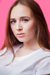 Closeup portrait of a beautiful young red haired girl on a pink background. A woman with clean skin and natural beauty