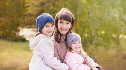 Fototapeta na wymiar Youn woman with two daughters. Outdoors. Autumn background. Mother day