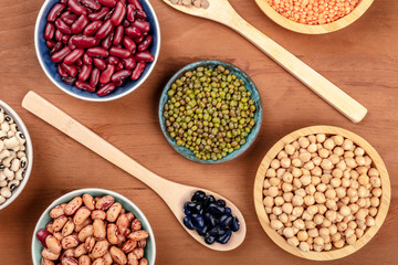 Various types of legumes, shot from above on a dark rustic wooden background. Red kidney beans, lentils, chickpeas, soybeans, black-eyed peas