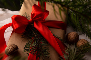 Prezenty bożonarodzeniowe. Świąteczny prezent zapakowany w ekologiczny papier przewiązany czerwoną kokardką, - obrazy, fototapety, plakaty
