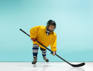 A hockey player in uniform with equipment over a blue studio background. The athlete, child, sport, action concept