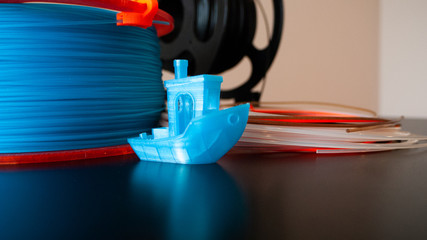 One blue 3D printed boat on a black surface with 3D printing filament in a variety of colors.