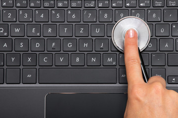 Woman hand is holding stethoscope on the keyboard of a laptop