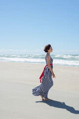 Beautiful brunette woman in a long dress walks along the seashore