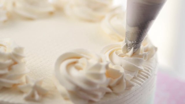 Confectioner topping cake with cream using pastry bag, slow motion.