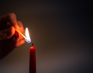 Close up of hand lighting red candle with match