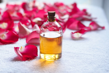 Obraz na płótnie Canvas Aromatherapy essential oil glass bottle among red rose petals on white terry towel. SPA and relax concept, selected focus
