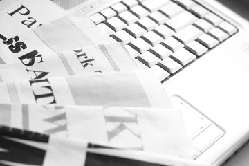 Newspapers and laptop. Pile of daily papers with news on the computer. Pages with headlines, articles folded and stacked on keypad of electronic device. Modern gadget and old journals, focus on paper