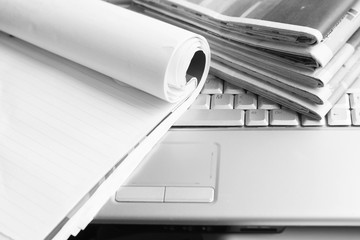 Business concept. Stack of fresh morning newspapers with business news and open paper notebook with blank sheets on keyboard of laptop, side view    