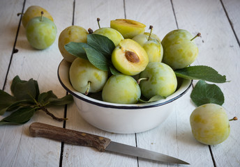 Fresh green plums in a bowl on white wooden table
