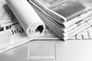 Newspapers and laptop. Pile of daily papers with news on the computer. Pages with headlines, articles folded and stacked on keypad of electronic device. Modern gadget and old journals, focus on paper