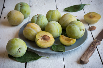 Fresh green plums on plate on white wooden table