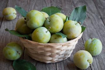 Fresh green plums in a basket on wooden background