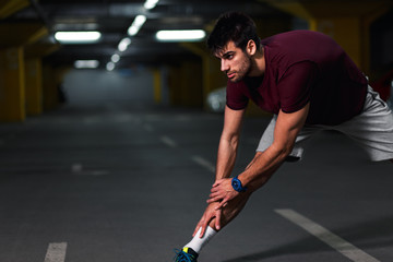 Young male runner stretching his muscles before workout in the underground car parking.