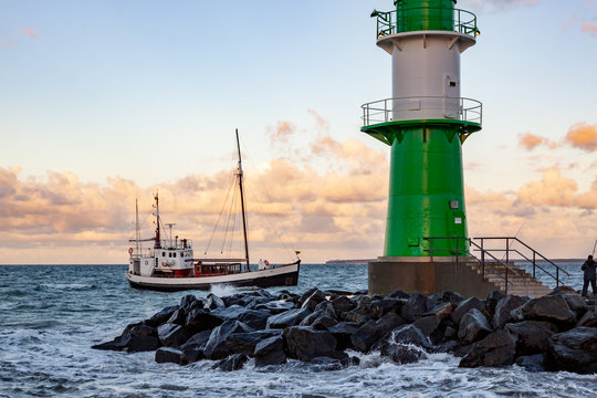 leuchtturm in der brandung mit fischerboot im hintergrund vor warnem&uuml;nde an der ostsee