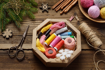 Fototapeta na wymiar Gift wrapping. Present for the needlewoman - thread, floss, needles, hook, cotton yarn. Composition with box, festive decoration and fir tree branch. Merry Christmas and Happy New Year concept