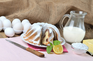 Obraz na płótnie Canvas Sliced homemade marble cake sprinkled with sugar, lemon, melissa, milk, eggs and butter