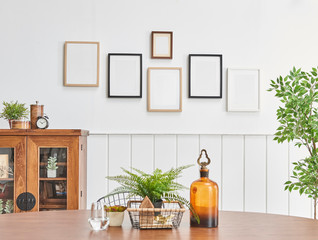 Wooden table close up and wooden cabinet background with many frames on the white wall.