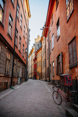 Fototapeta na wymiar Gamla Stan. Stockholm, Sweden. Colorful street in Old Town. Color street with cobblestone road, orange houses, streetlight and bicycle. Perspective of the Narrow street.