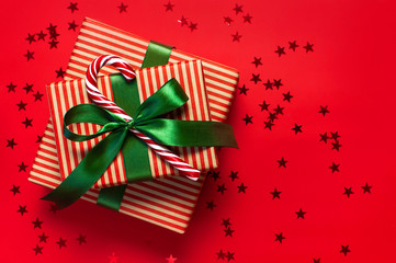 Gift boxes with green ribbon, Candy Cane, glitter confetti form of stars on red background top view...