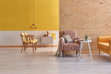 Modern living room with brick wall and yellow wall background style. Wooden furniture detail chair and grey cabinet.
