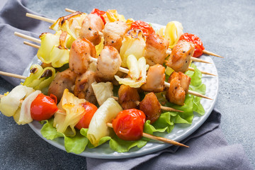 Kebab chicken, zucchini and tomatoes on skewers in a plate. Dark table