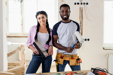 happy young couple with tools looking at camera while making renovation of home
