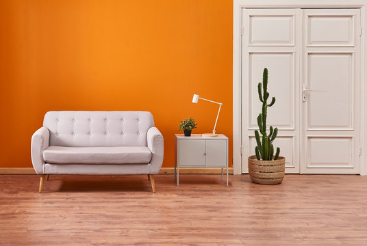Orange room, white door, grey sofa and white lamp decoration.