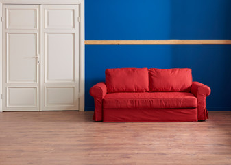 Dark blue wall and wooden banner on the wall, red sofa with white classic door.