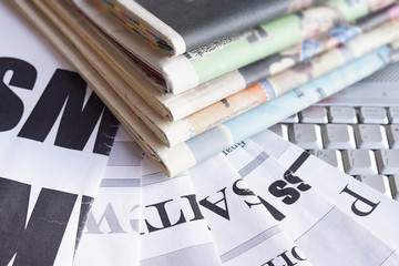 Newspapers and laptop. Pile of daily papers with news on the computer. Pages with headlines, articles folded and stacked on keypad of electronic device. Modern gadget and old journals, focus on paper 