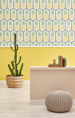 Decorative pineapple wallpaper, yellow wall, interior concept room with cactus and grey puff.