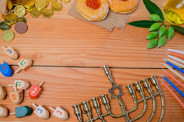 Top view of jewish holiday hanukkah celebration with menorah (traditional candelabra), wooden dreidels (spinning top), donut, olive oil and chocolate coins on wooden table.
