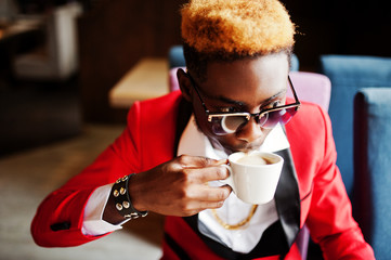 Obraz premium Fashion african american man model at red suit, with highlights hair and sunglasses sitting at cafe with coffee.