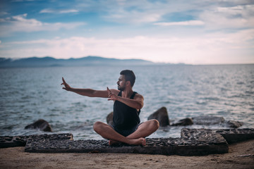 Fototapeta na wymiar Young man doing yoga by the sea. A handsome guy is sitting on the ocean at sunset.