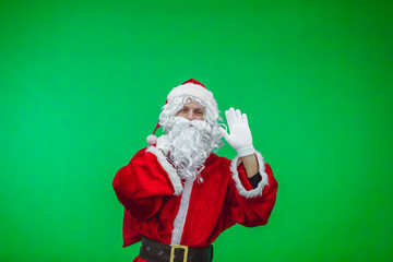 Merry Christmas. Santa Claus in a red suit carries a bag with gifts, waving his hand on a green screen background chromakey