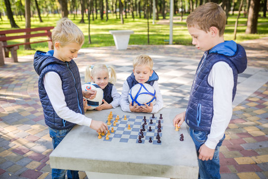 The topic children learning, logical development, mind and math, miscalculation moves advance. large family brothers and sister Caucasian boys and girl playing chess park bright sunny weather autumn