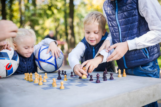 The topic children learning, logical development, mind and math, miscalculation moves advance. large family brothers and sister Caucasian boys and girl playing chess park bright sunny weather autumn