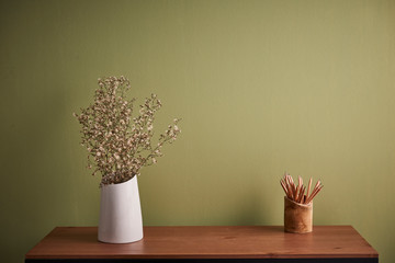 Green wall background, wooden desk and white vase of flower. Wooden pencil.