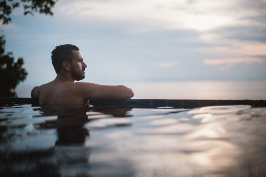 Portrait Of A Young Handsome Man In An Outdoor Pool. Attractive Guy With A Beard At The Side Of The Pool