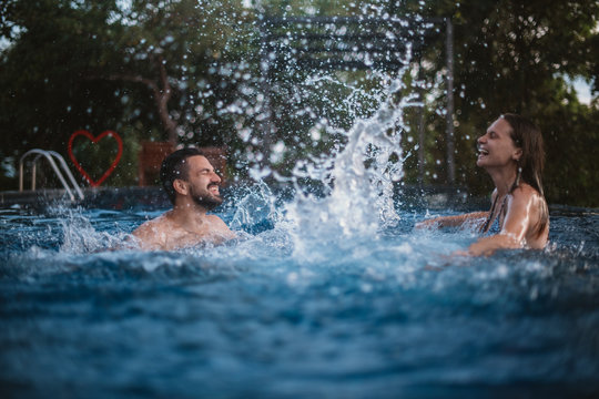 Young couple playing in the outdoor pool. Loving couple splashing water