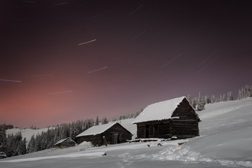Winter night with old wooden huts in the mountains