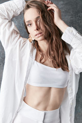 Sexy brunette female model posing in white shirt, top and pants. Studio shot, grey background