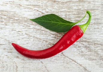 Fresh ripe chili pepper pod with leaf on the old shabby wooden background.  