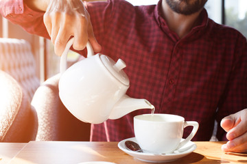 A man pours tea from a teapot in a cafe
