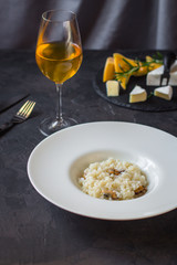 risotto with mussels (seafood rice) in a white plate and a glass of white wine on a dark background
