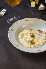 risotto with mussels (seafood rice) in a white plate and a glass of white wine on a dark background