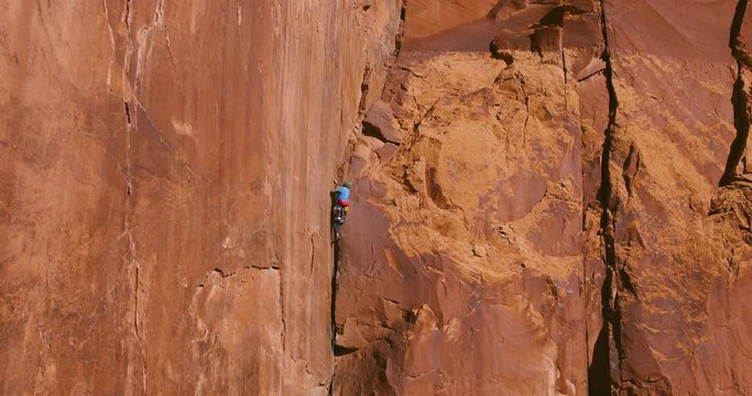 Aerial view of man rock climbing extreme route reaching for hand hold