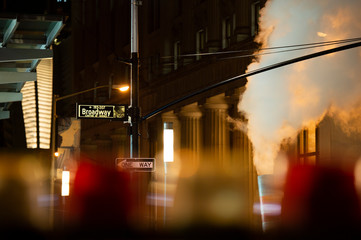 (selective focus) Broadway sign illuminated at night in Manhattan, New York. Steam coming out of the manhole on the right side. - obrazy, fototapety, plakaty